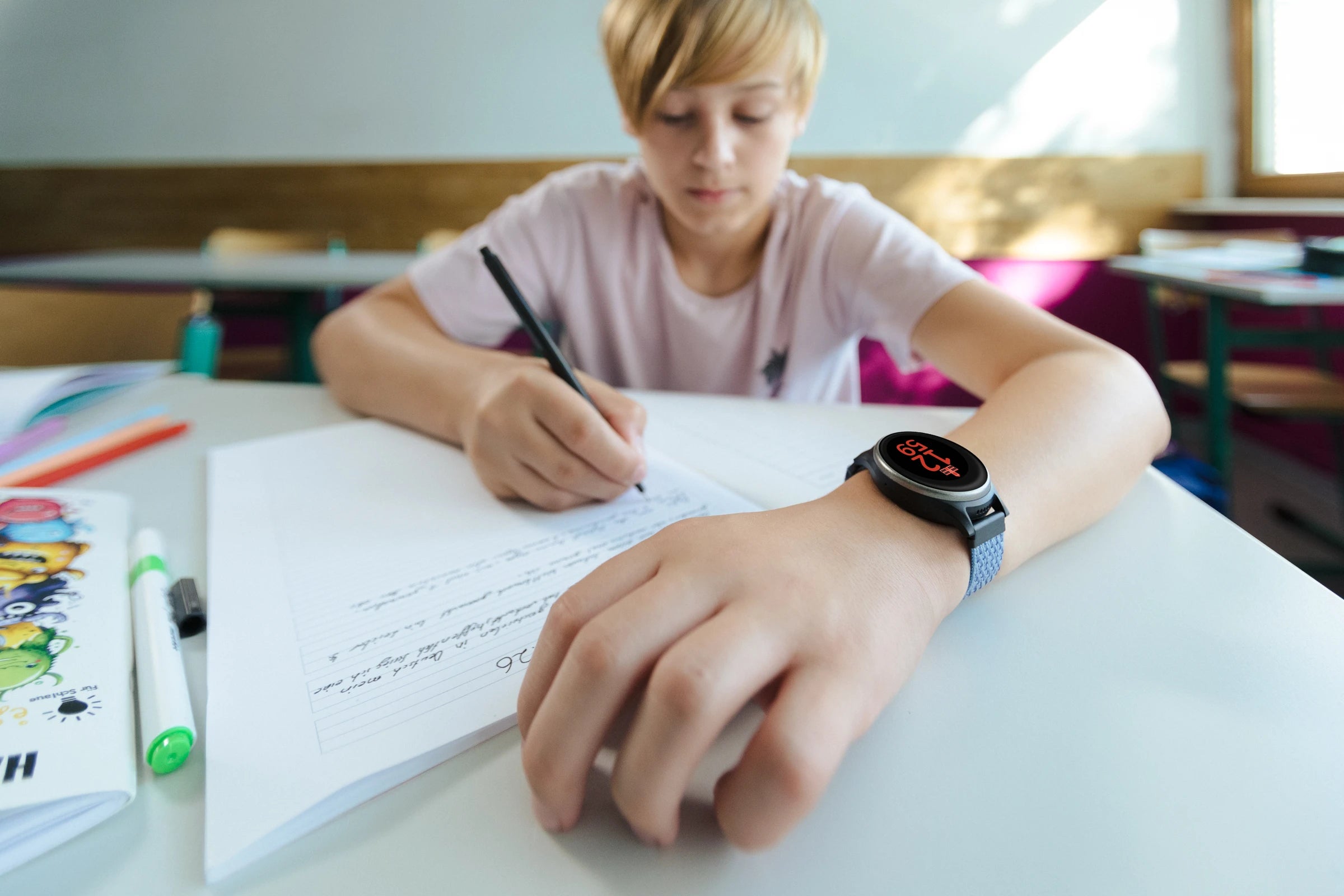 Kind mit Anio Uhr beim Schreiben in der Schule